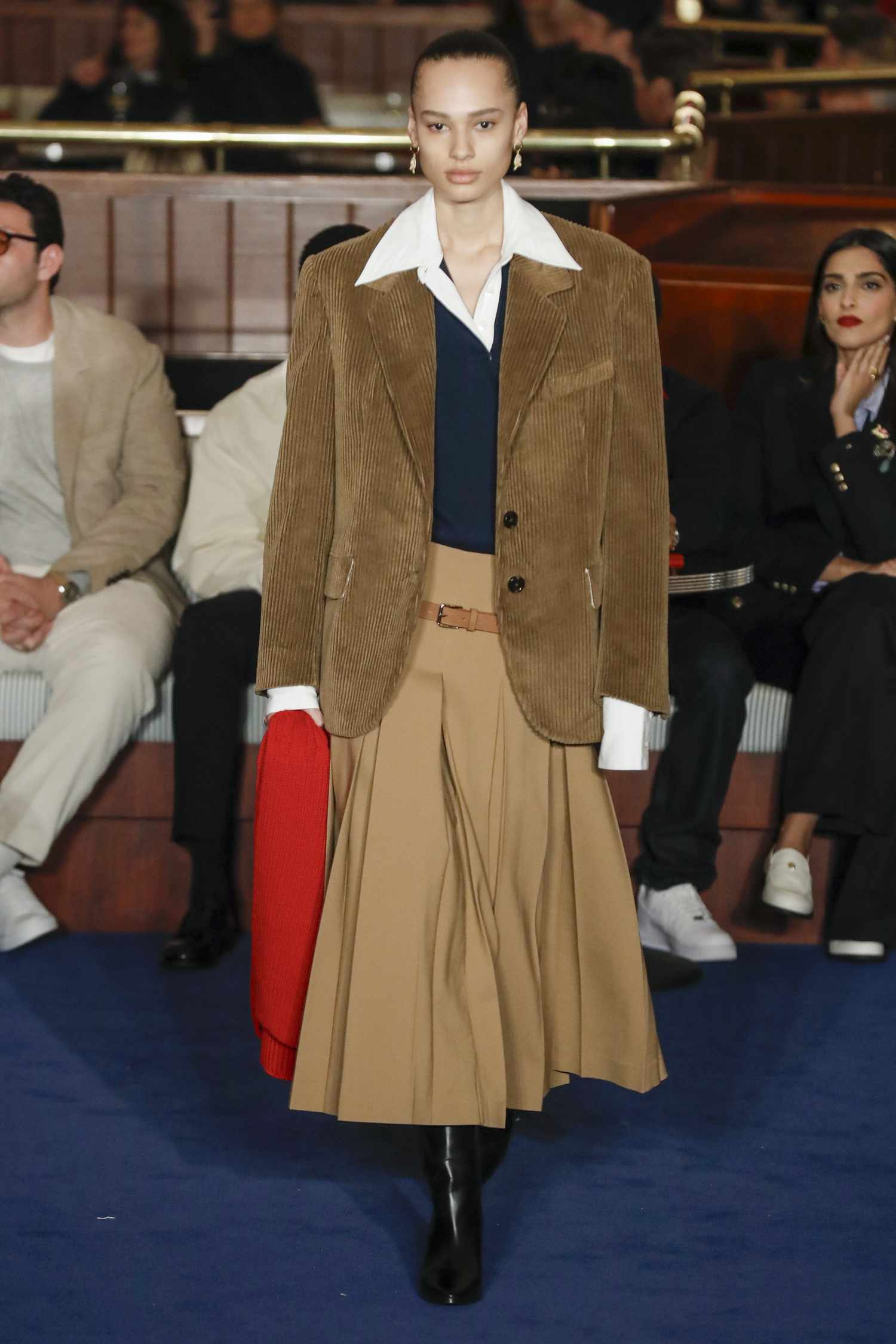 A model walks the runway wearing a layered look with a collar peeking out of the tan blazer. 