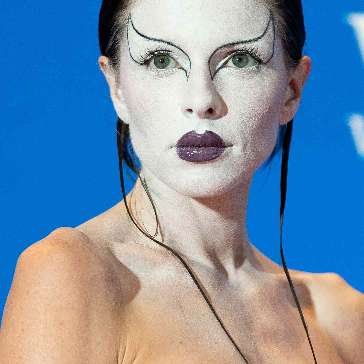 Julia Fox wearing white makeup with thin black wings outlining both eyes and purple lipstick