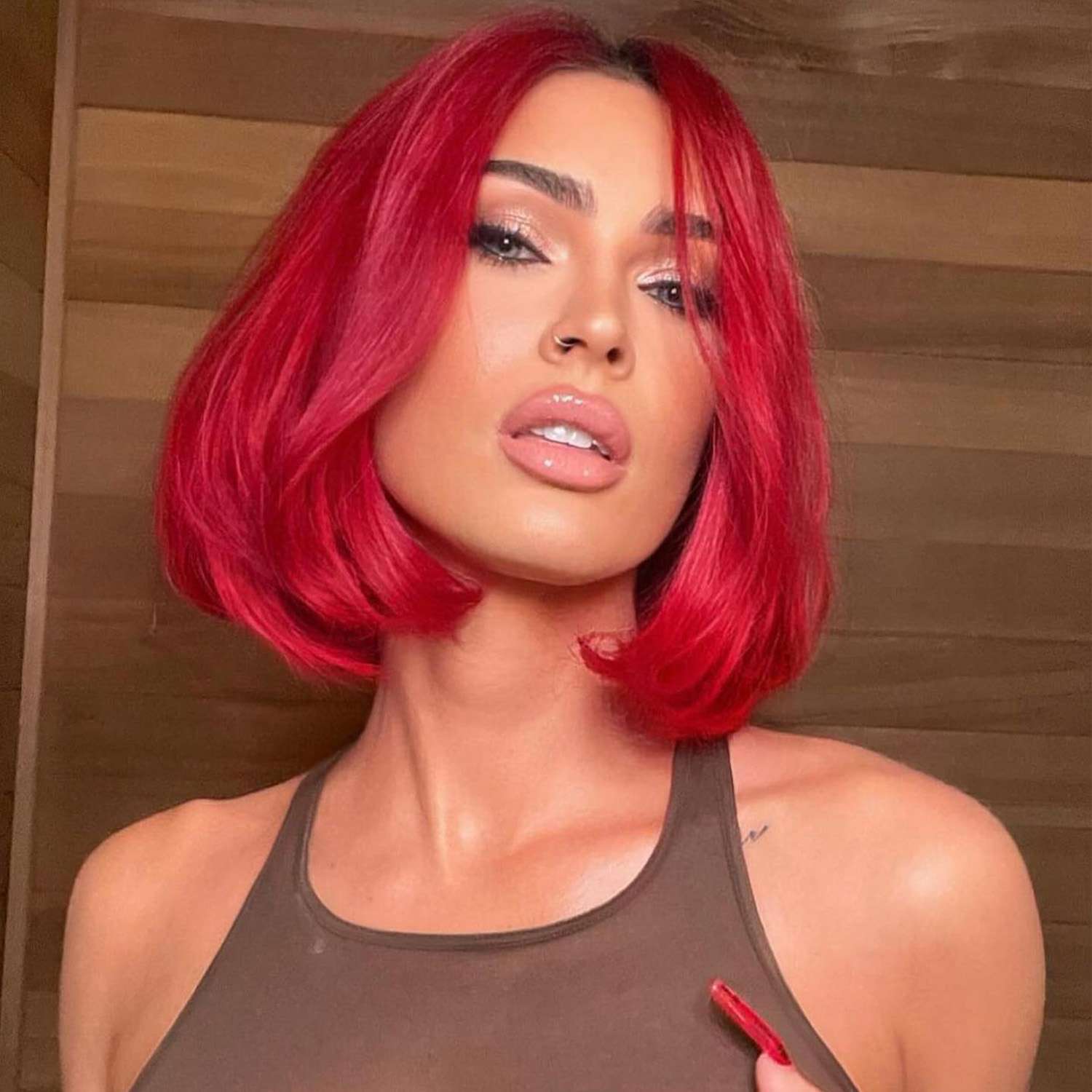 Megan Fox with a mushroom shaped fiery red bob, glittery eyeshadow, and a tan tank top