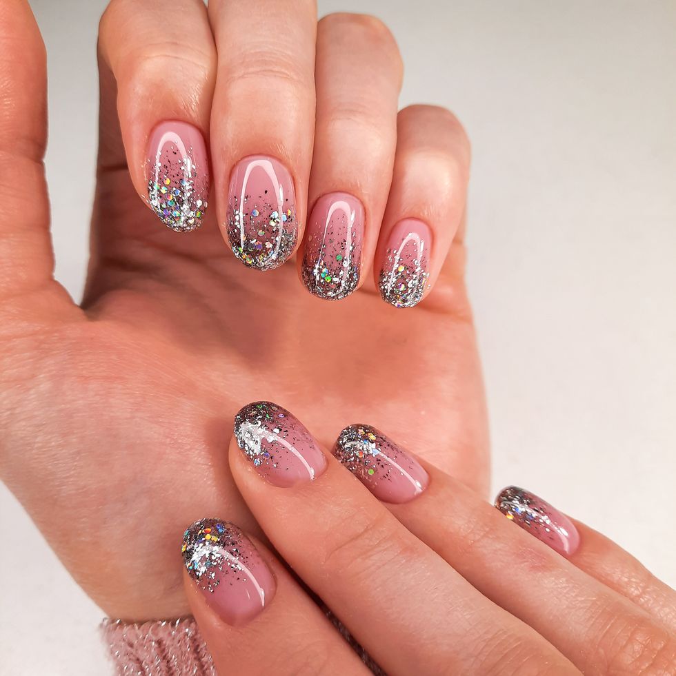 delicate camouflage coating with silver design hands in a sweater with pink gel polish and sequins stylish and shiny nail polish coating