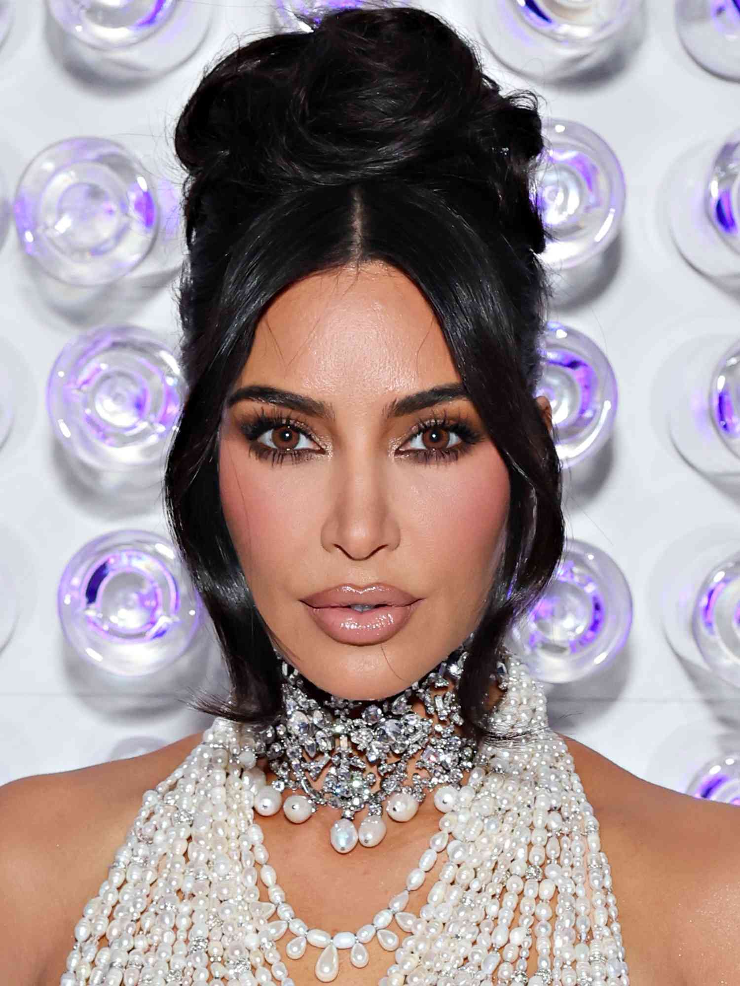 Kim Kardashian wears layered pearl necklaces, high updo, and brown smokey eye and nude lip