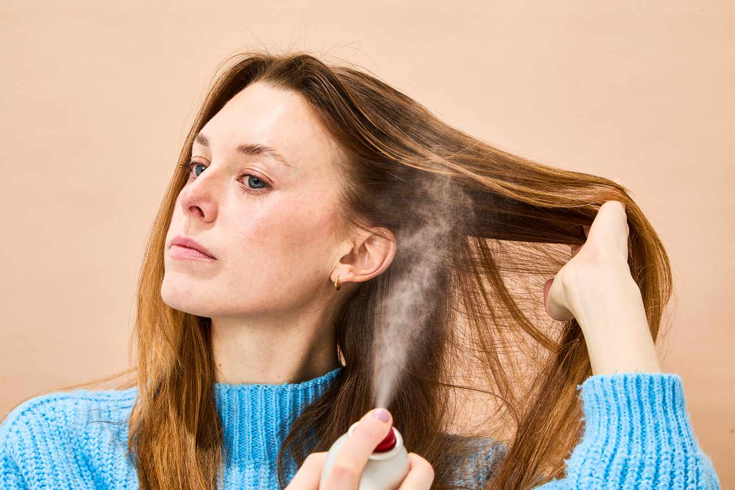 A person spraying their hair with Kenra Perfect Medium Spray 13