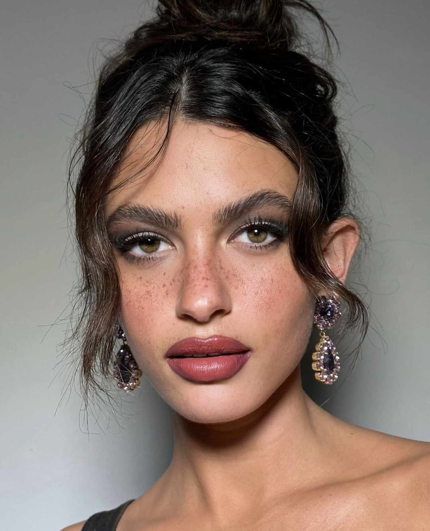 woman wearing smoky eyeshadow with black liquid eyeliner and creamy rose lipstick with prominent freckles