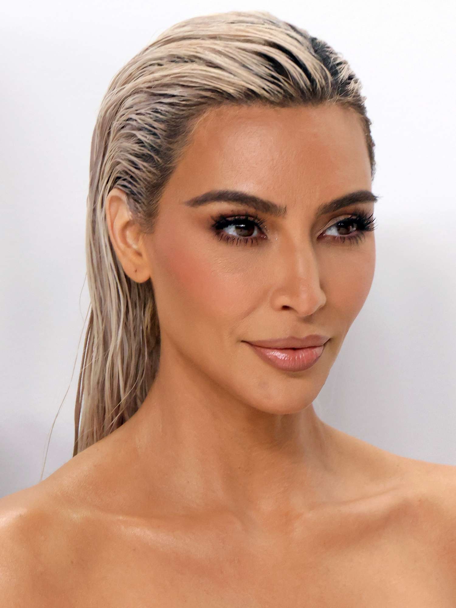 Kim Kardashian with slicked-back platinum hair, bronzed skin, nude pink lipstick, blush, and mascara