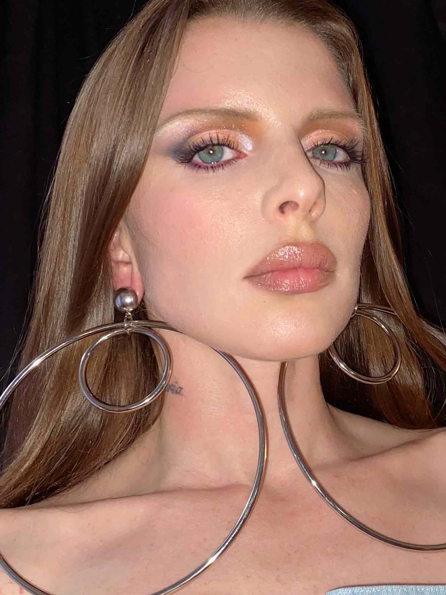 Julia Fox with thin blonde '90s brows, a radiant makeup look, and oversized silver earrings