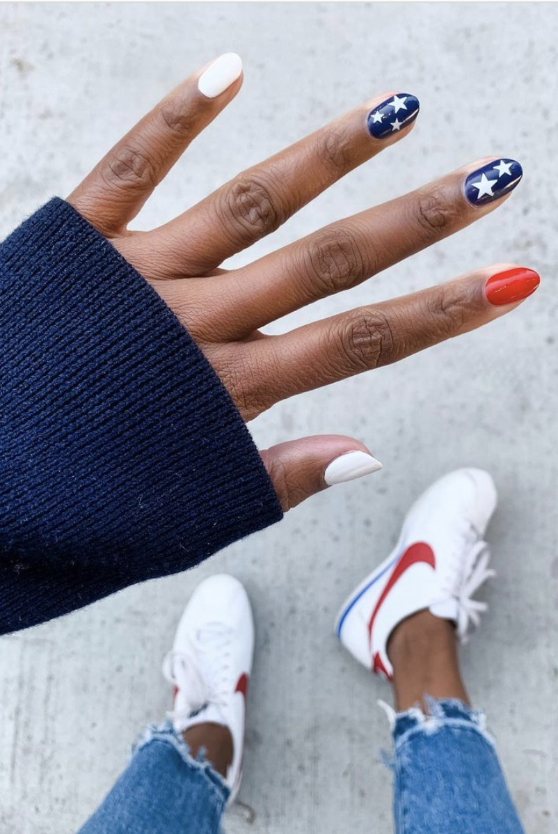 a manicure that features various designs on each fingernail, like a white base, a blue base with a few white stars and a red base