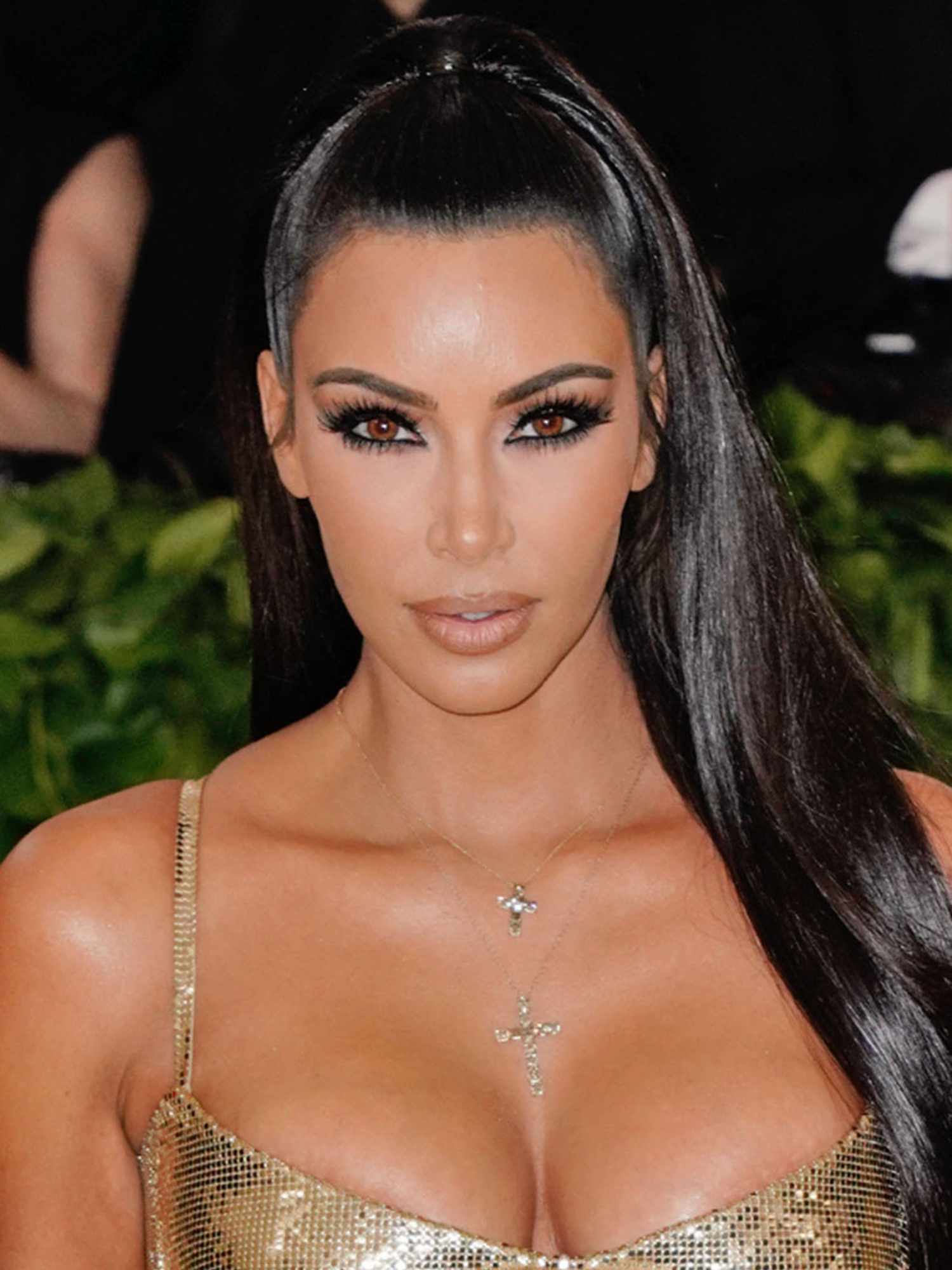 Kim Kardashian wearing gold dress, half-up half-down hairstyle, and '90s-inspired makeup with thin brows, mascara, and nude lipstick