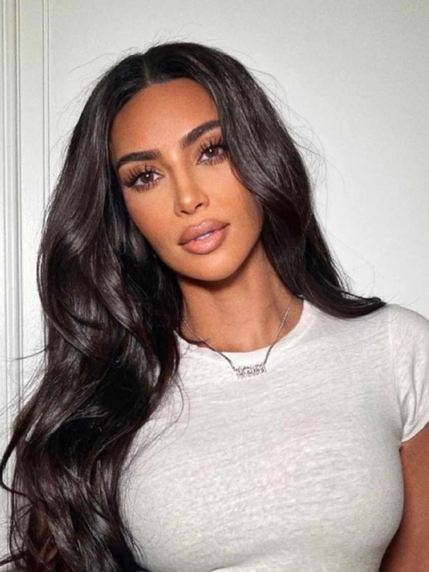 Kim Kardashian wearing gray t-shirt, long, wavy hairstyle, lots of mascara, and nude pink lipstick 