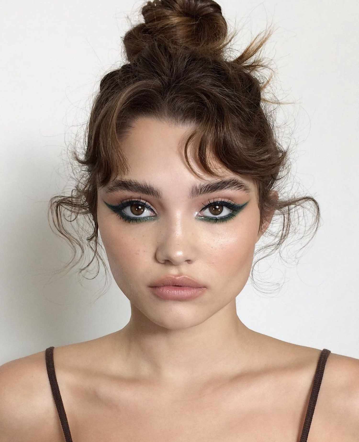 woman wearing deep green eyeliner on the bottom lashline in a wing style with sheer nude lips