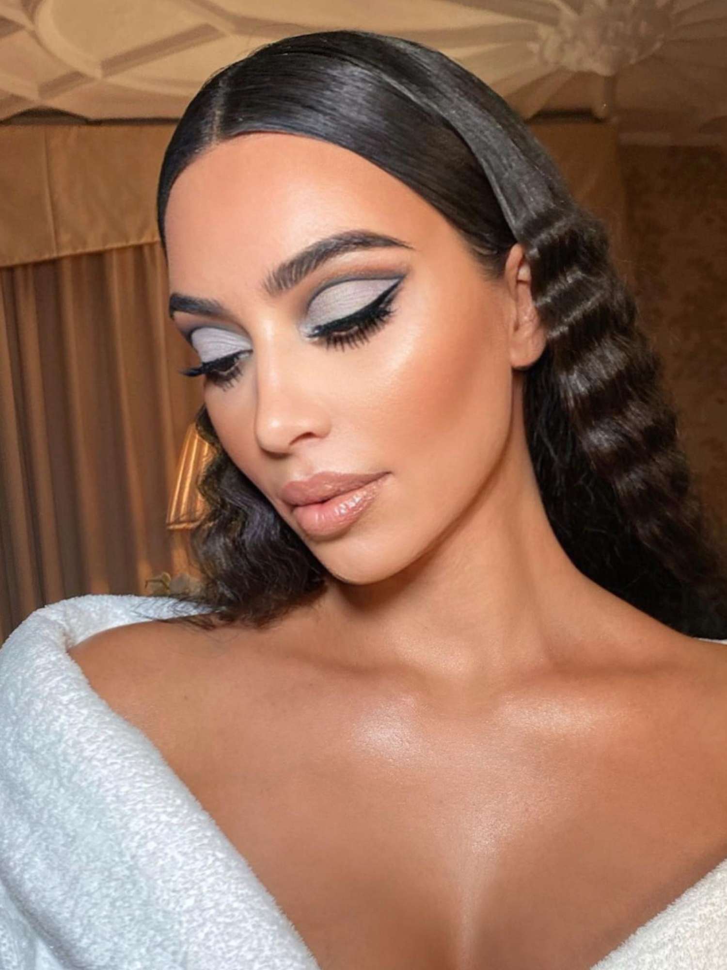 Kim Kardashian with wavy hairstyle tucked behind ears, gray cut-crease eye makeup, and glossy nude lip