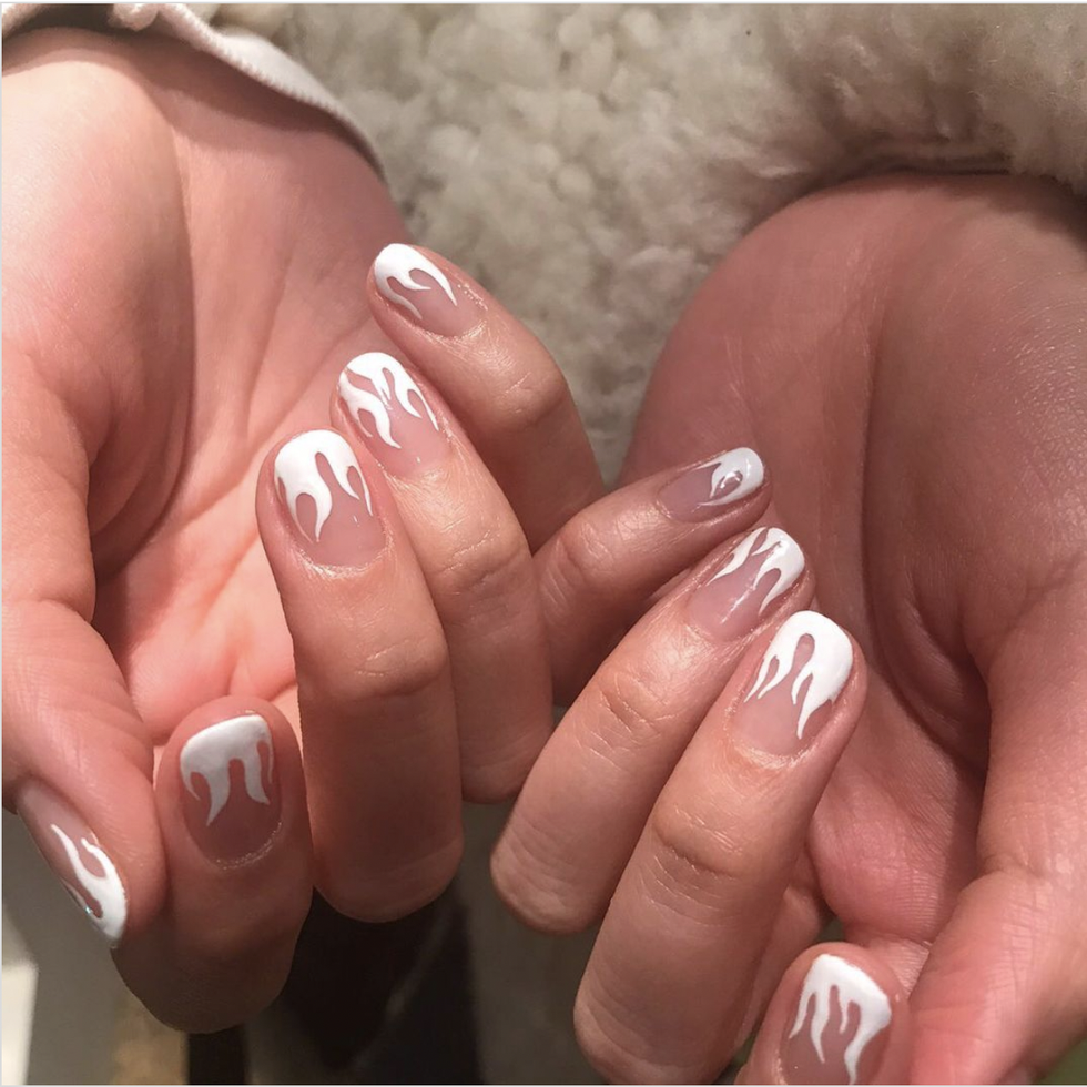 hands in sweater with knitted sleeves and with nude color manicure with gold glitter on pink table