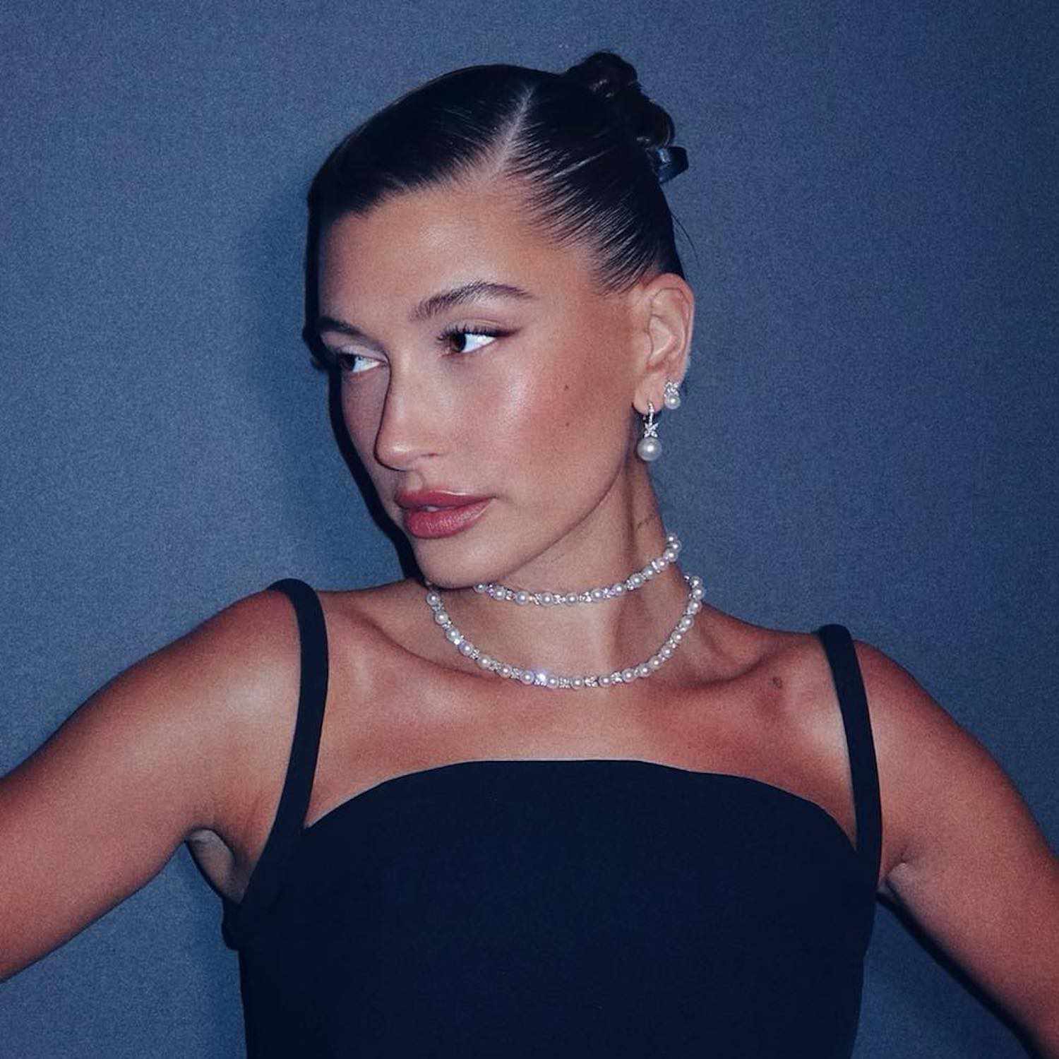 Hailey Bieber wears an Audrey Hepburn-inspired look with slick updo, little black dress, and pearls