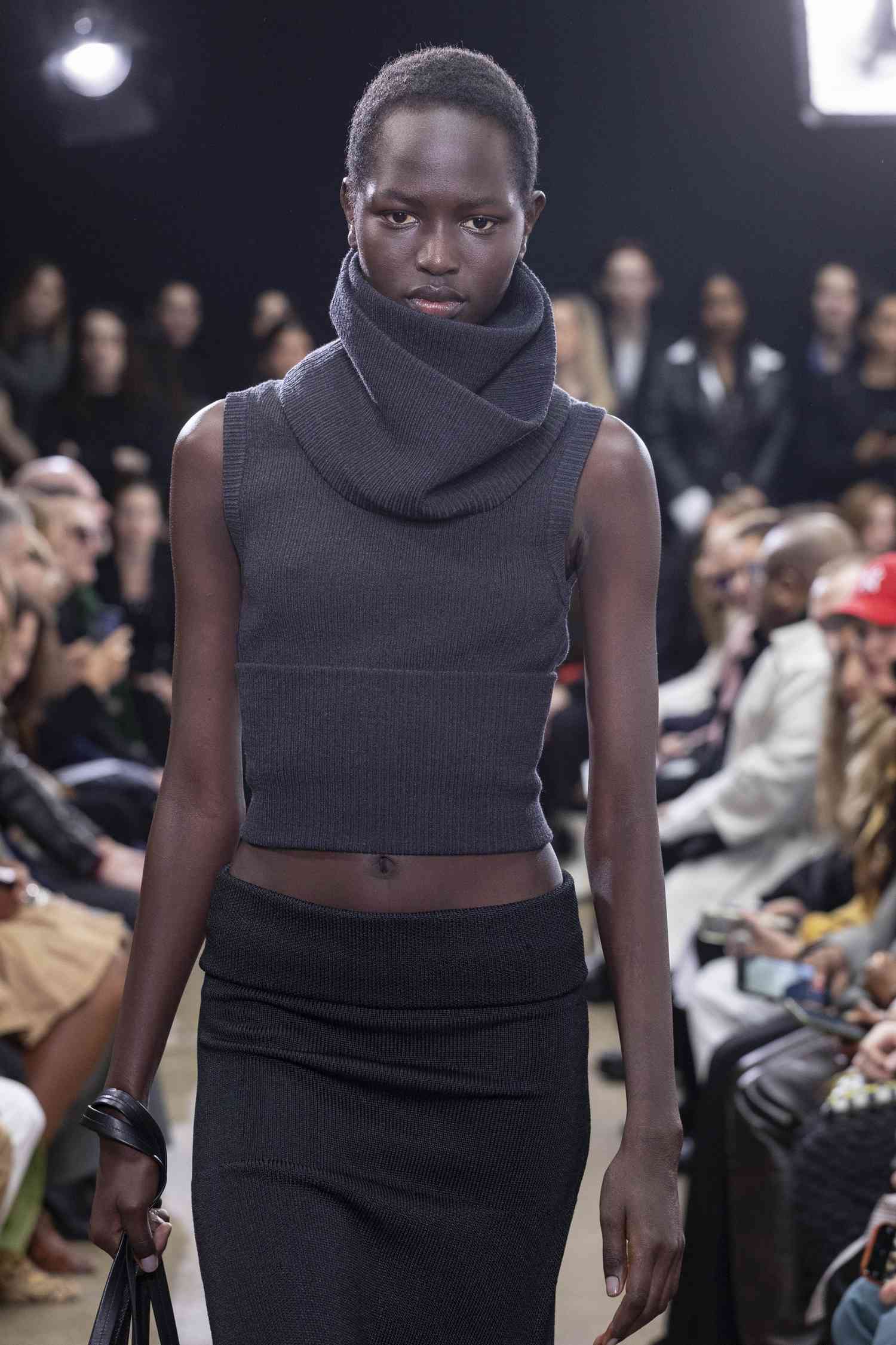 A model walks the Proenza Schouler runway show wearing a tank top with a turtle neckline and black skirt.