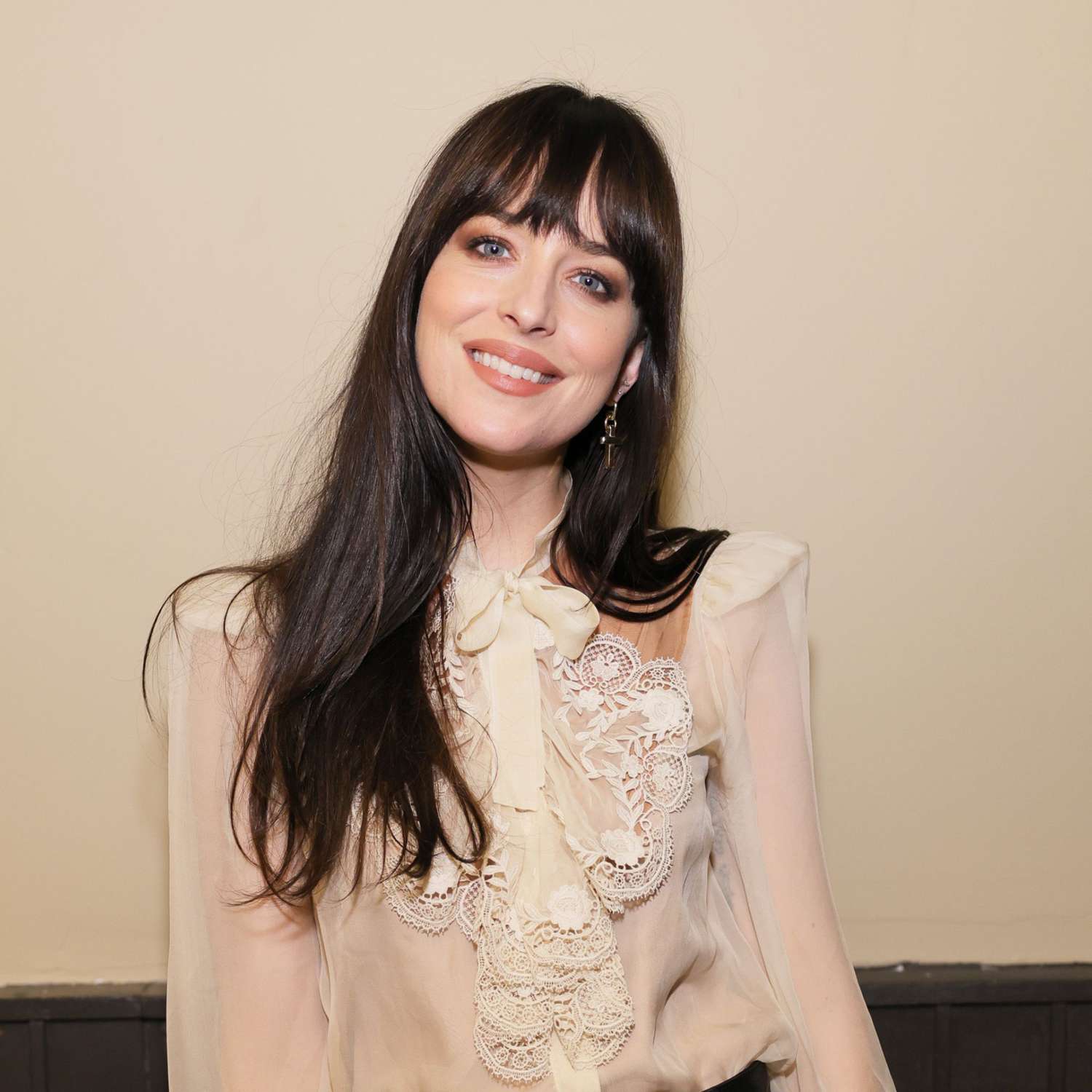 Dakota Johnson with wispy bangs and a lacy blouse with oversized bow