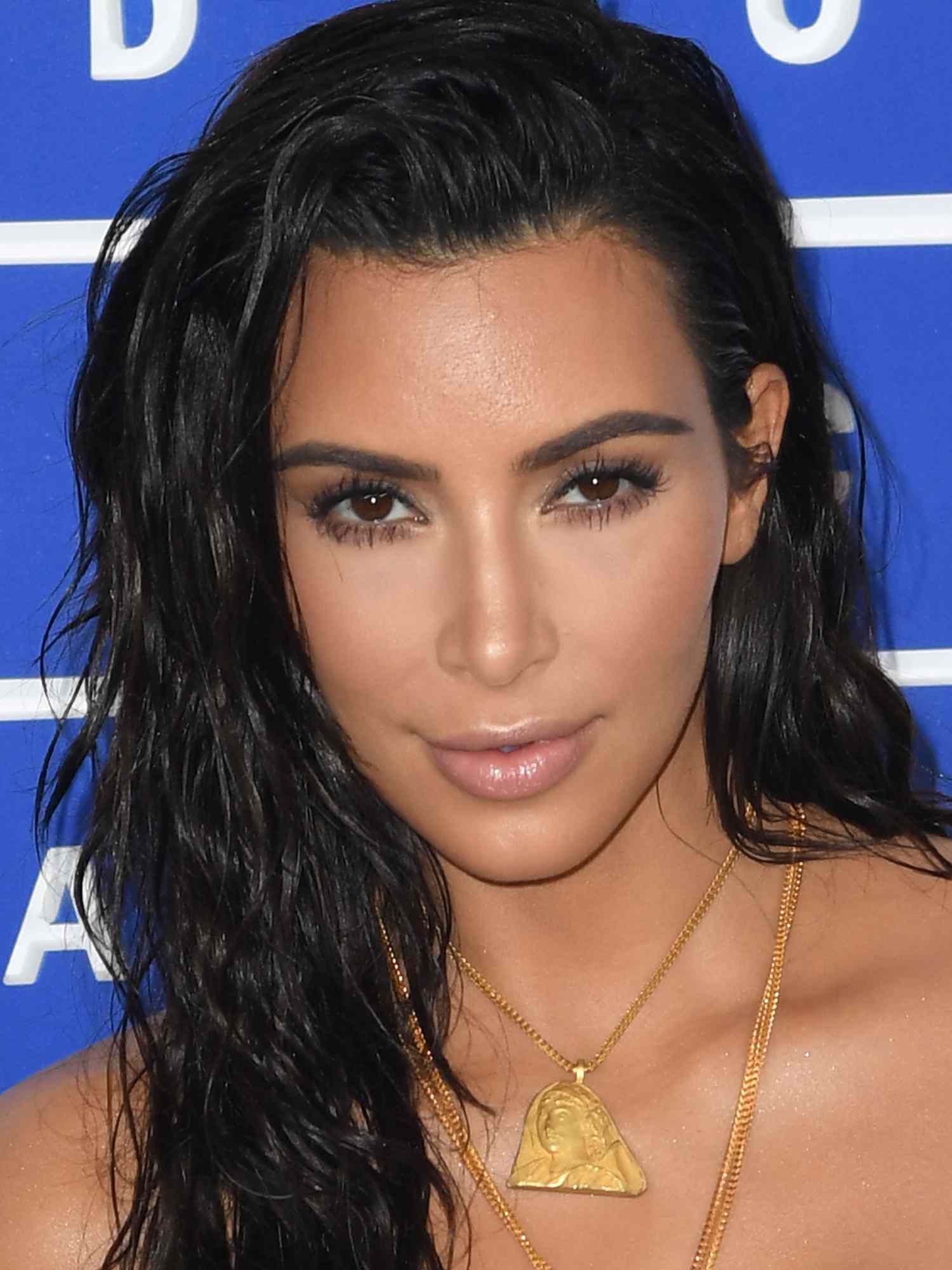 Kim Kardashian with a side-parted beach waves hairstyle, bold eyebrows, dewy skin, and nude lipstick