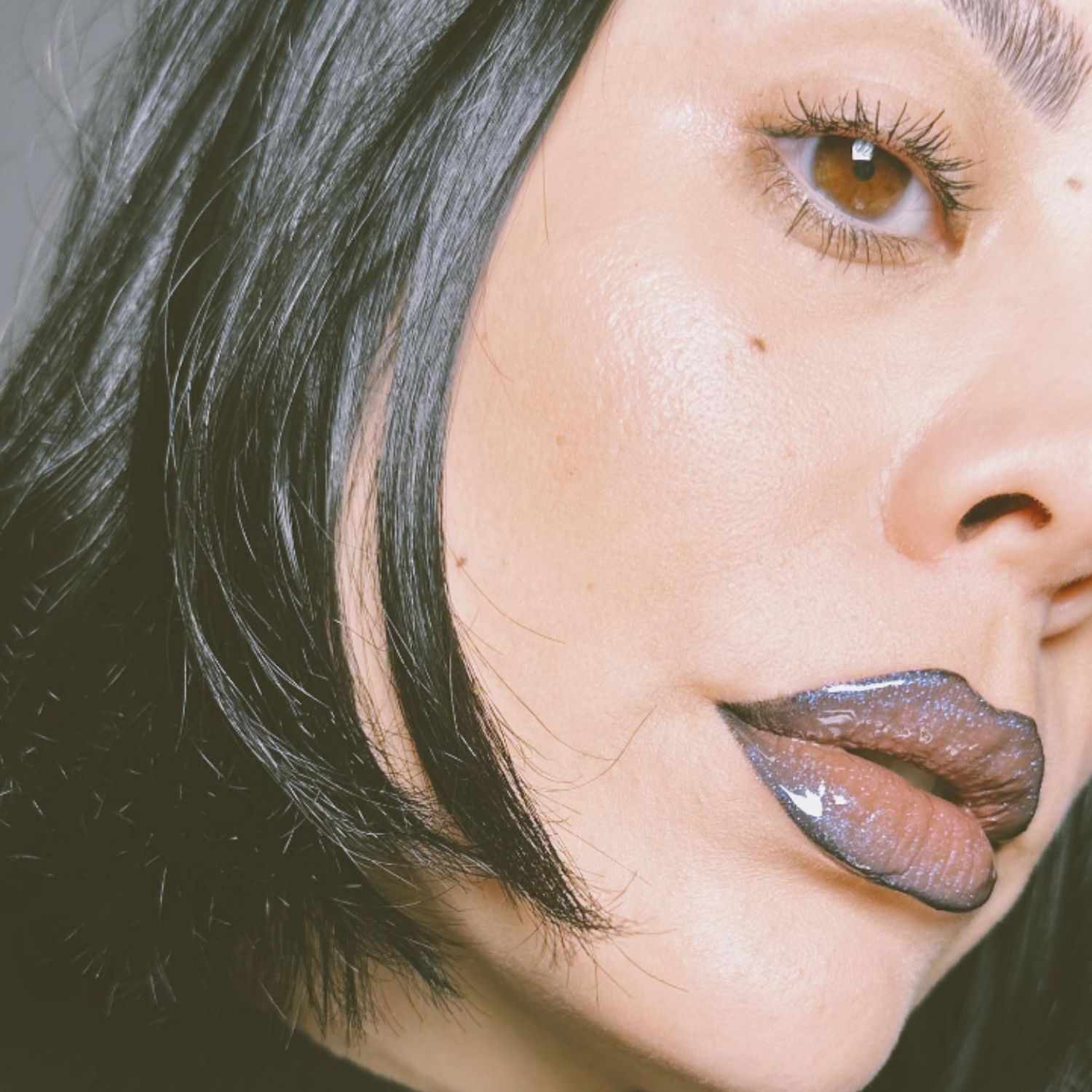 Lips lined in black with glossy, sparkle-y dark-hued gloss on top.