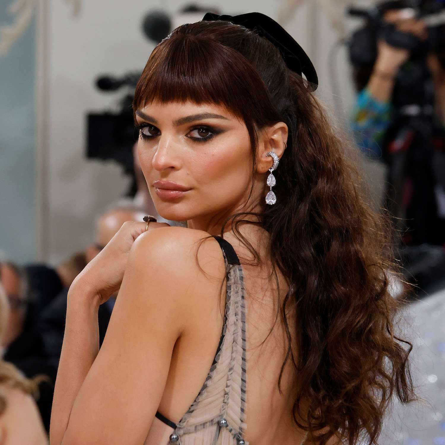 Emily Ratajkowski wears a half-up hairstyle with a black bow, baby bangs, and cascading curls to the 2023 Met Gala