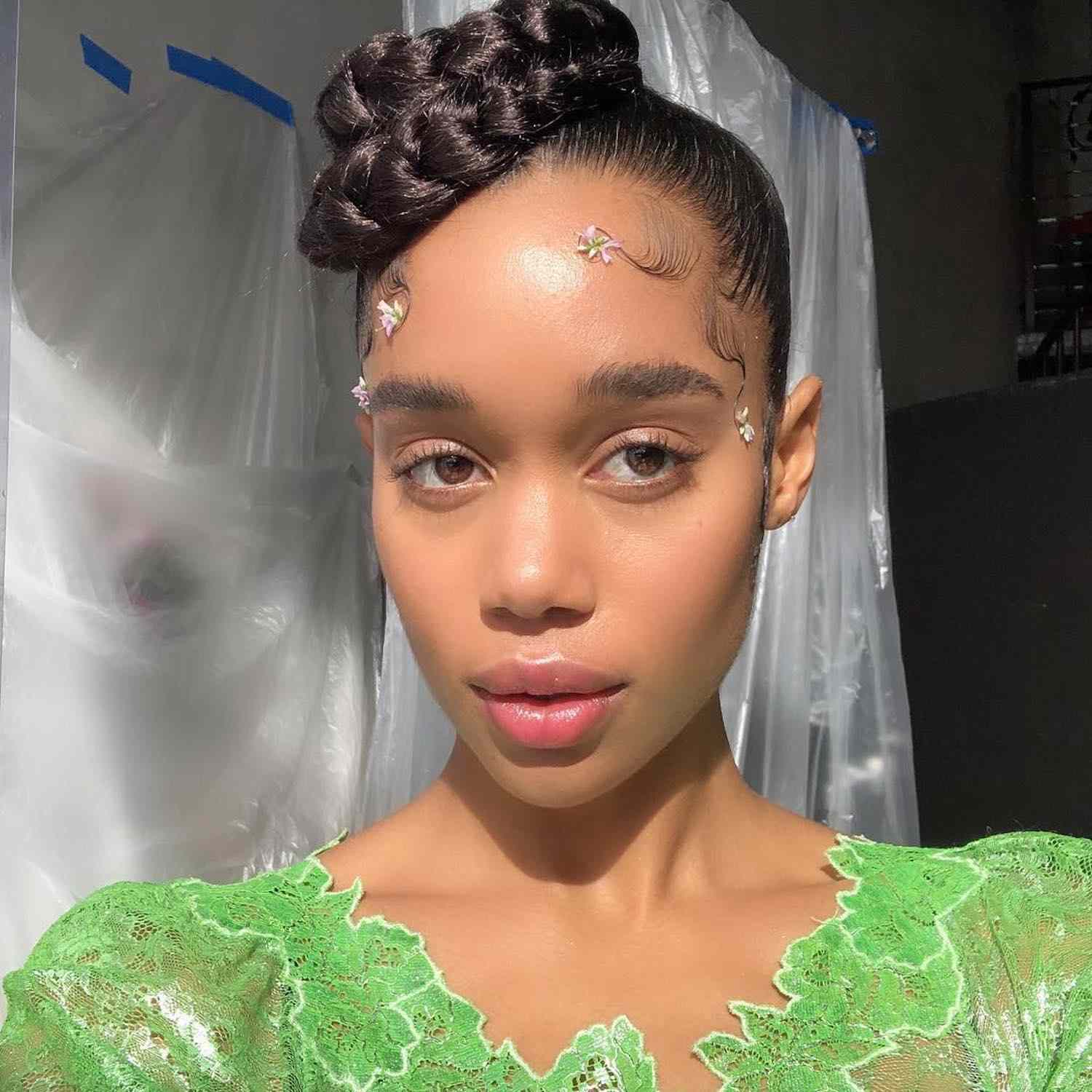 Laura Harrier wears a braided topknot hairstyle with baby hairs and flowers