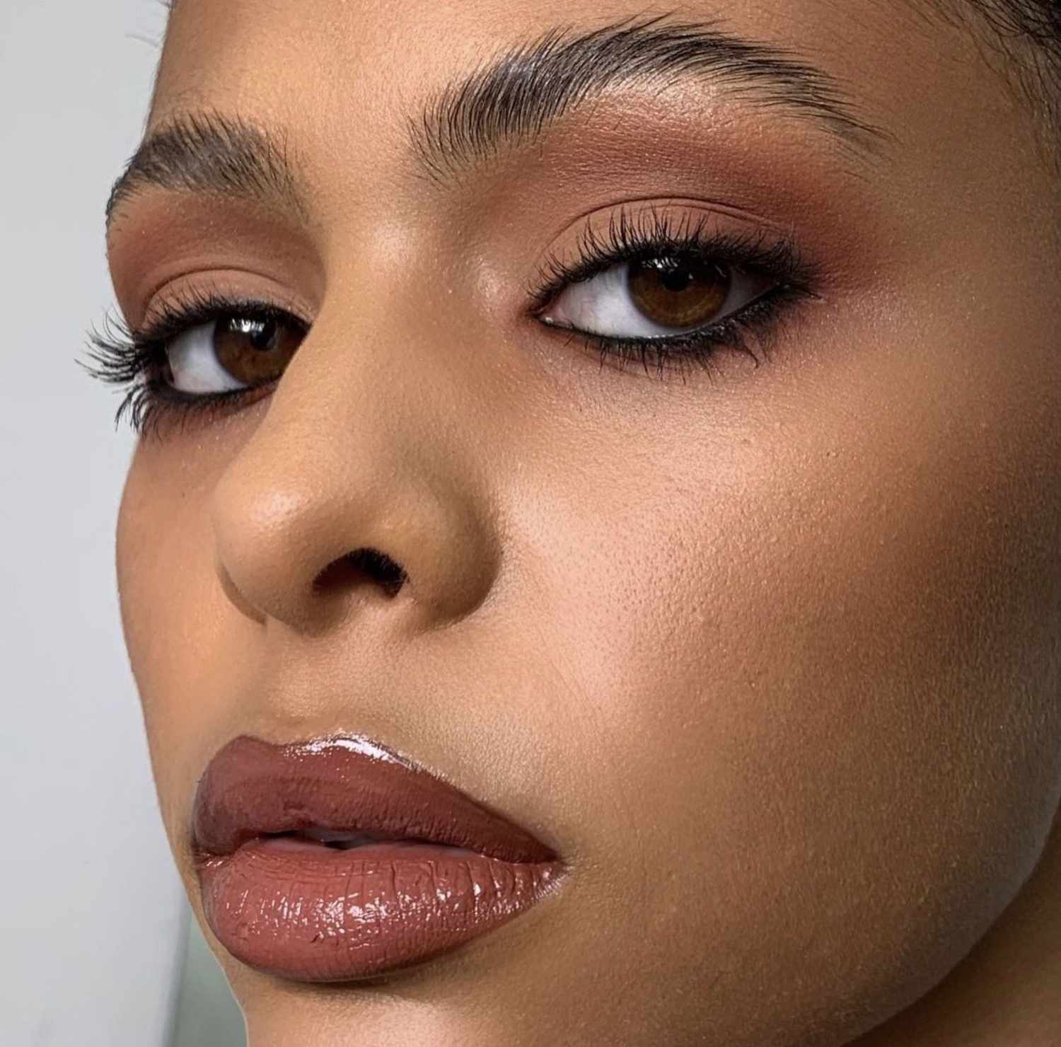 woman wearing warm brown tones on the eyes with intense black eyeliner lining both the top and bottom and a mocha brown and pink toned lipstick with a glossy finish