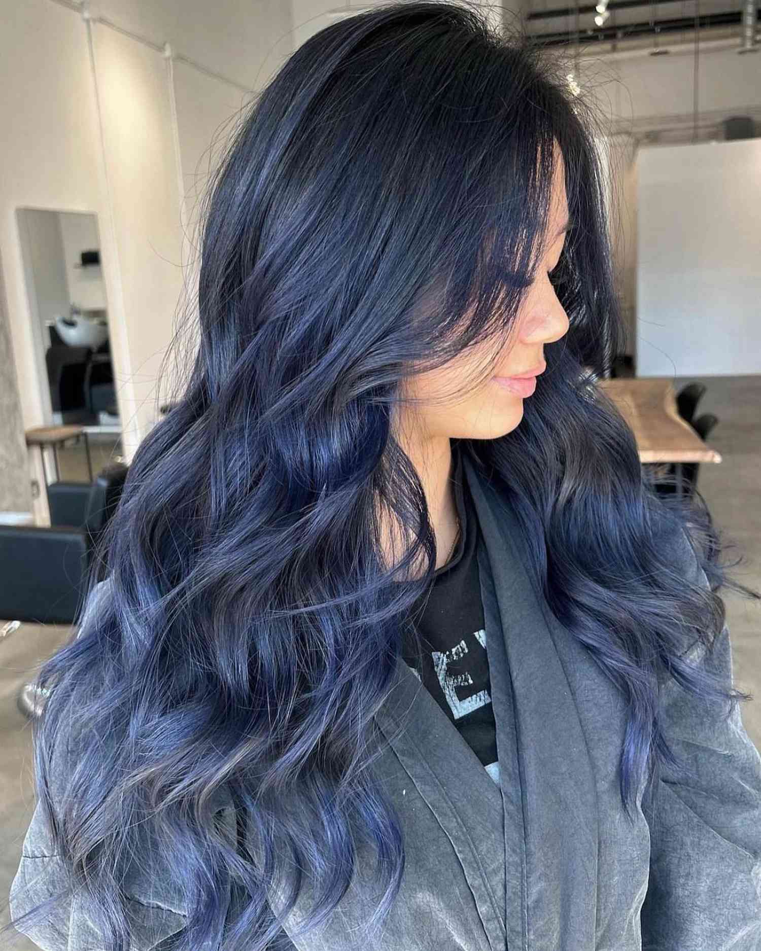 Close up of a woman with blue-black hair in barrel waves, turned in profile.