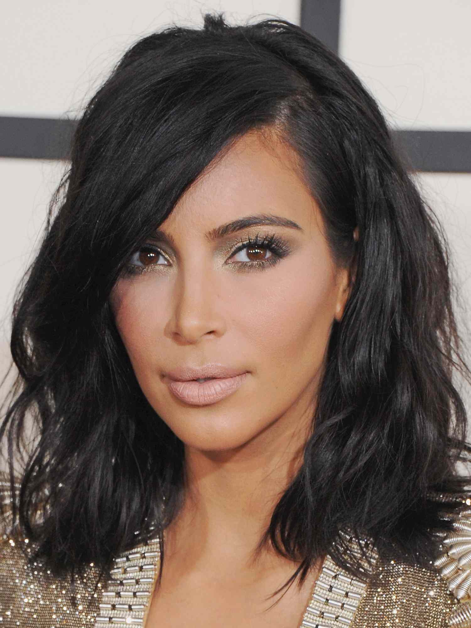 Kim Kardashian with a black wavy long bob hairstyle, gold shimmer eyeshadow, and pale nude lipstick