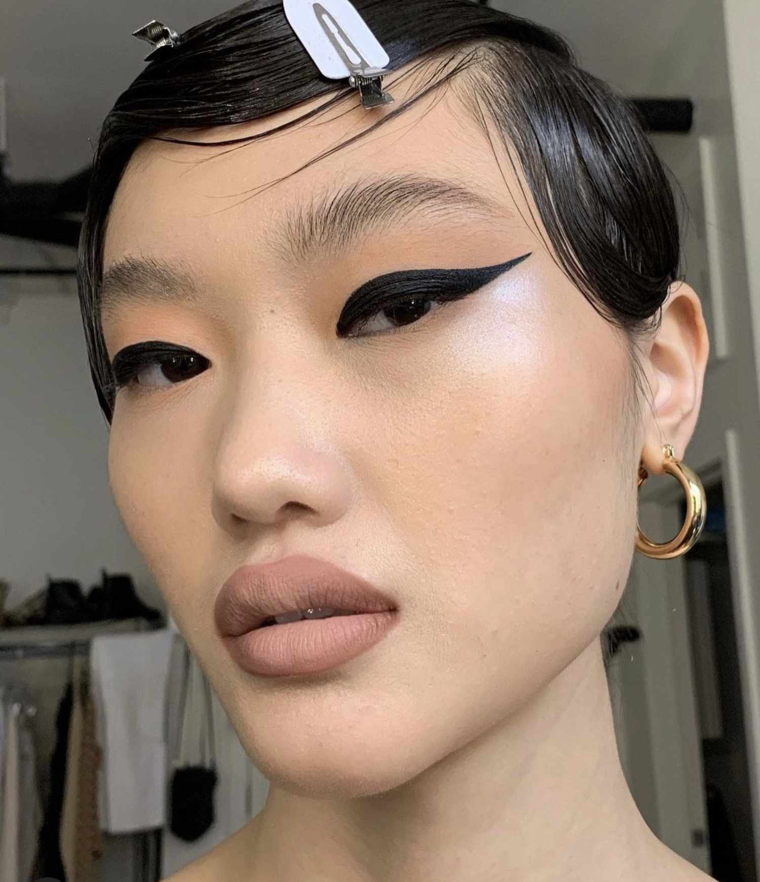 woman wearing a graphic wing liner on the top lashline and a matte nude lipstick