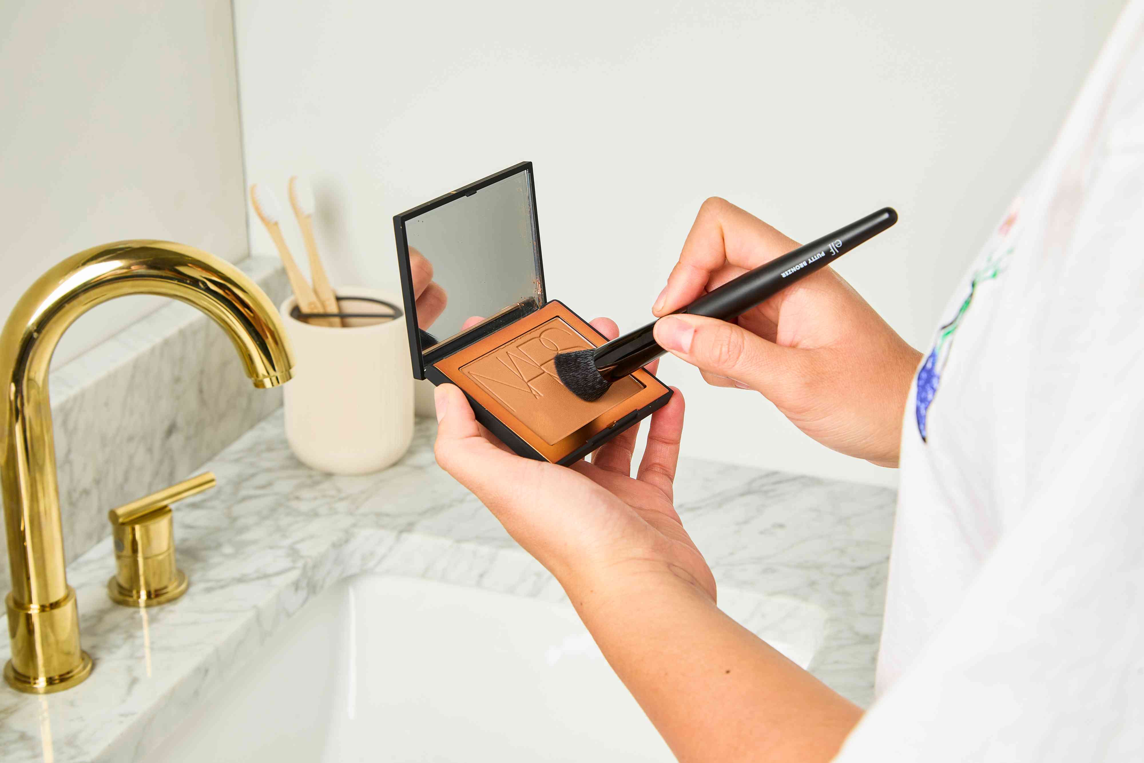 A person applies NARS Laguna Bronzing Powder with a makeup brush