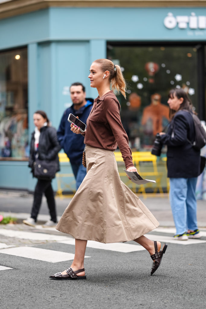 PARIS, FRANCE - SEPTEMBER 30: A guest wears dark brown long sleeve shirt, light brown midi skirt, black belted slingback Ganni leather shoes, dark brown pattern bag, outside Stella McCartney, during the Paris Fashion Week Spring/Summer 2025 on September 30, 2024 in Paris, France.