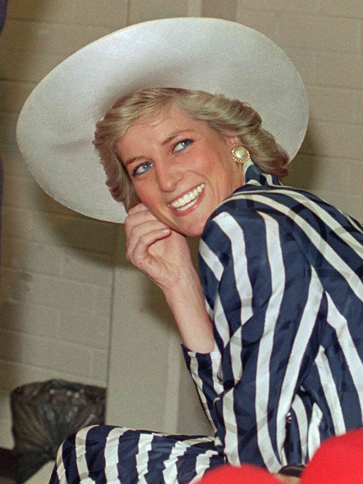 Princess Diana wears a feathered haircut, wide-brimmed white hat, and blue and white striped dress