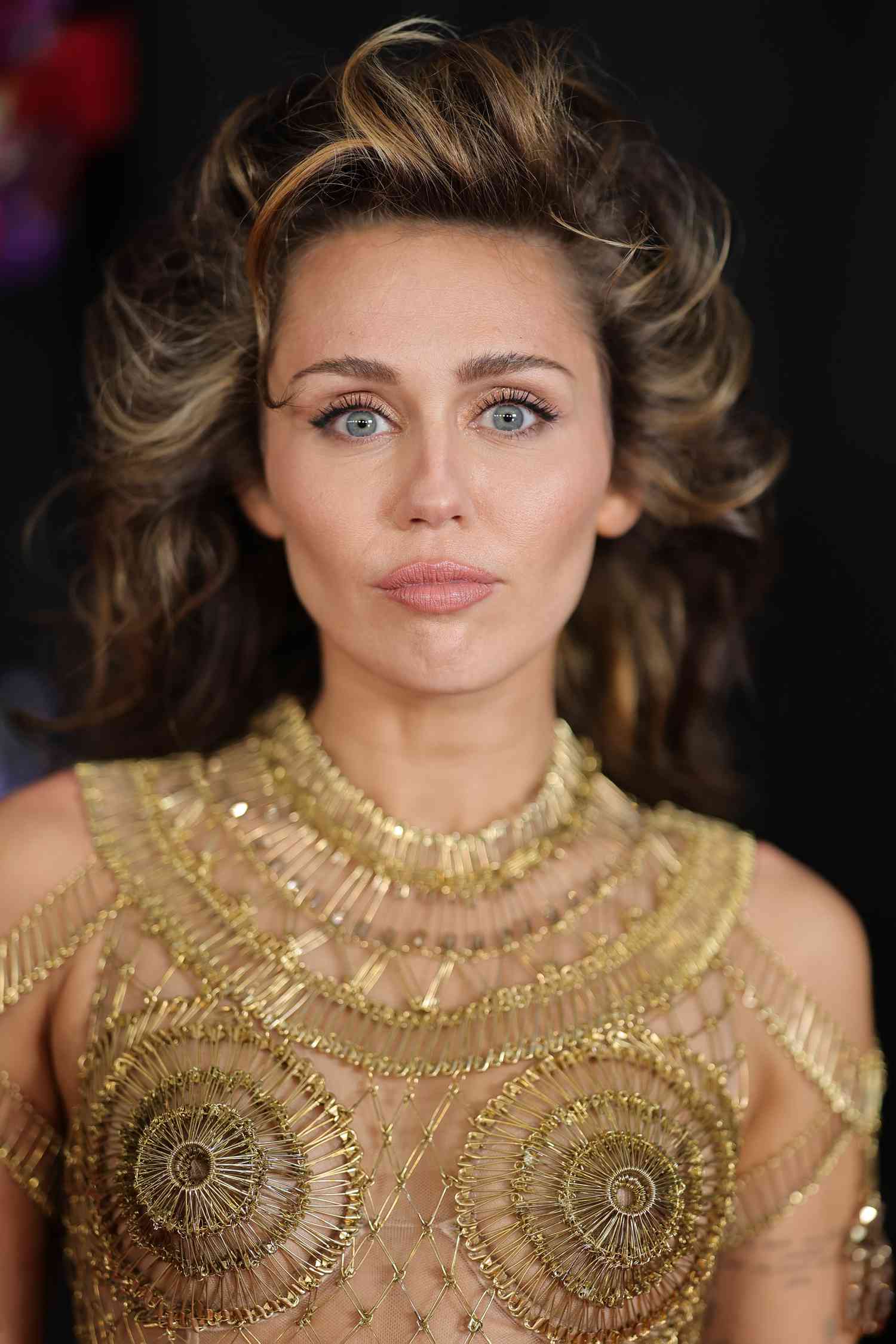 Miley Cyrus at the 2024 Grammys with a golden goddess inspired makeup look, Maison margiela dress, and voluminous swept back blowout.