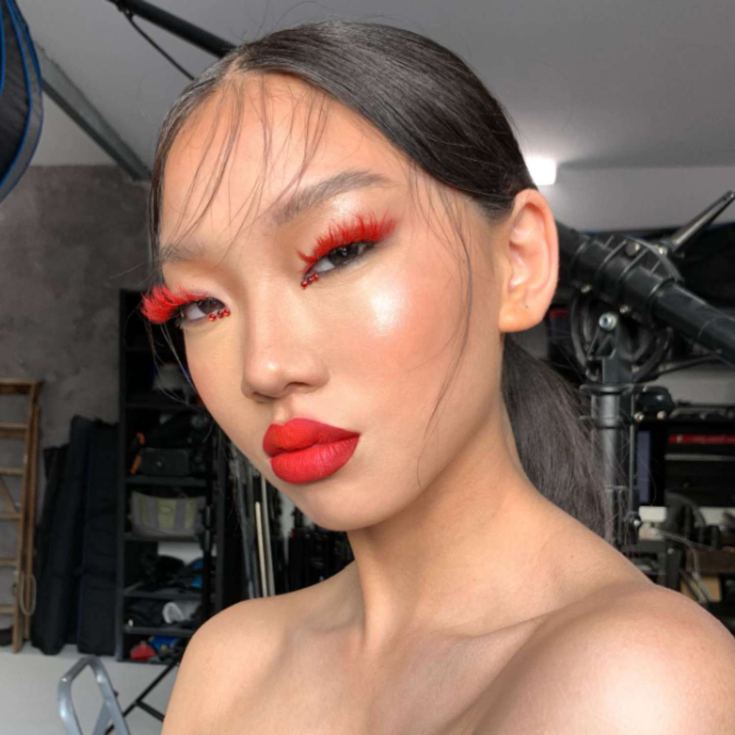 Red fake lashes, red gems in the inner corners of the eye, and a bold ombre red lip.