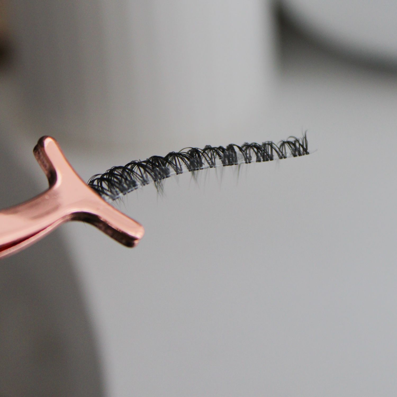 Kiss My Lash But Better false lash strip held in rose gold tweezers