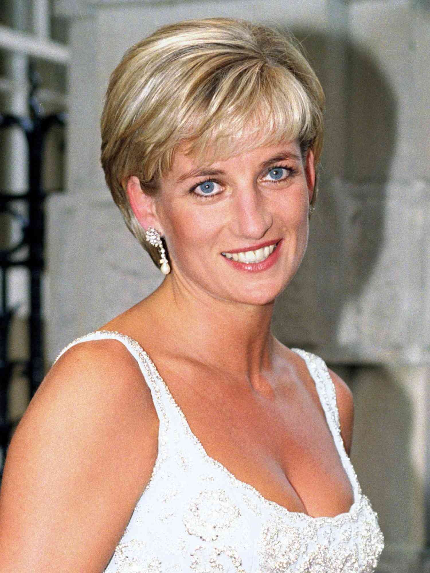 Princess Diana wears a sleek long pixie cut with bangs, pearl drop earrings, and blue dress with white beading