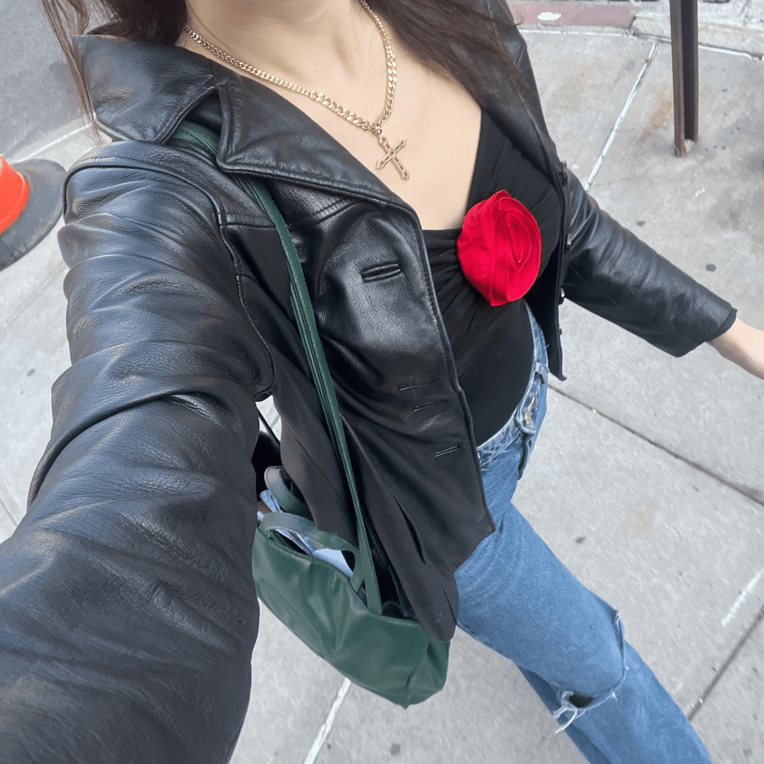 A below the neck shot of Byrdie news director Madeline Hirsch wearing a black leather jacket, a black shirt with a red rosette detail, and light wash jeans.