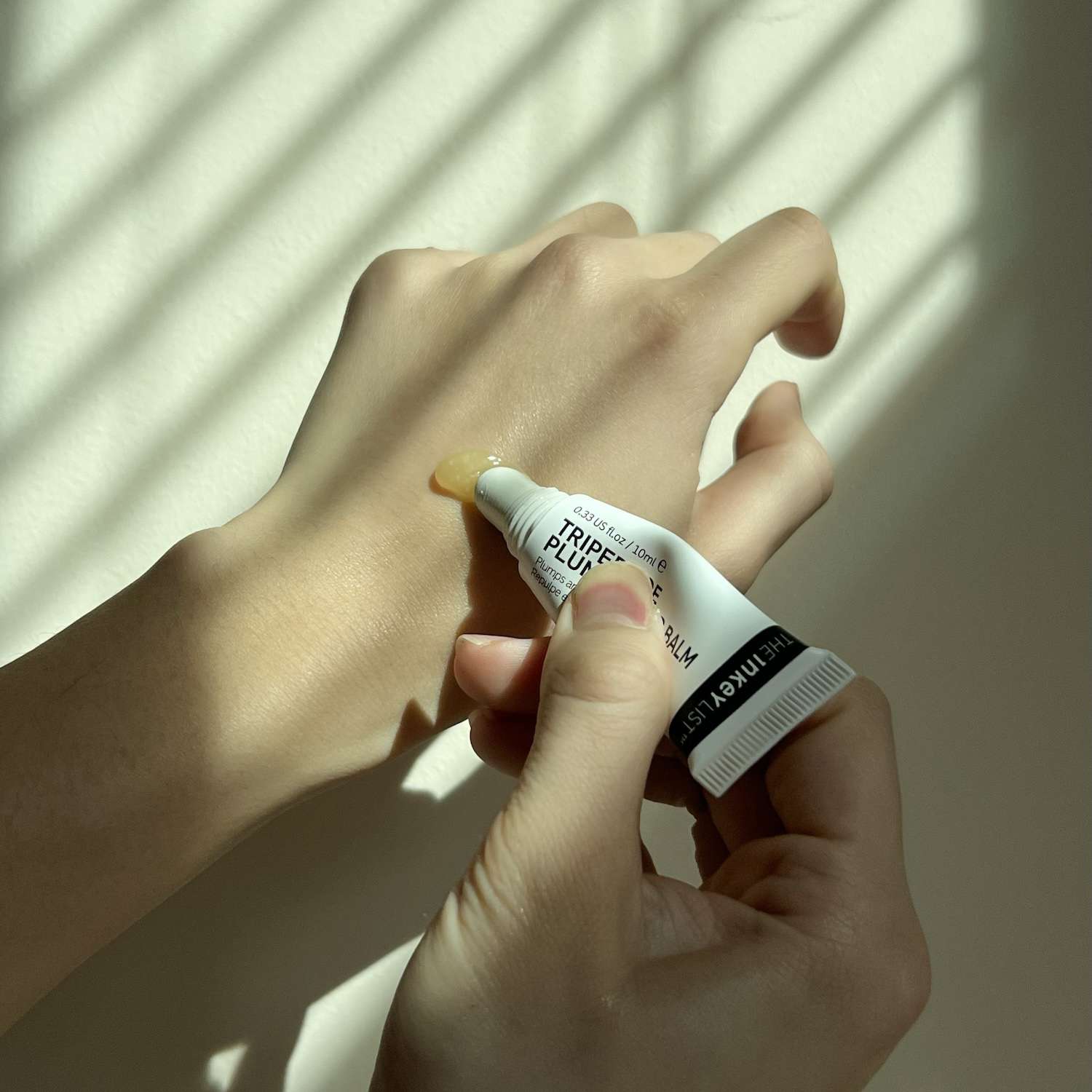 Close-up of applying The Inkey List's Tripeptide Plumping Lip Balm to hand