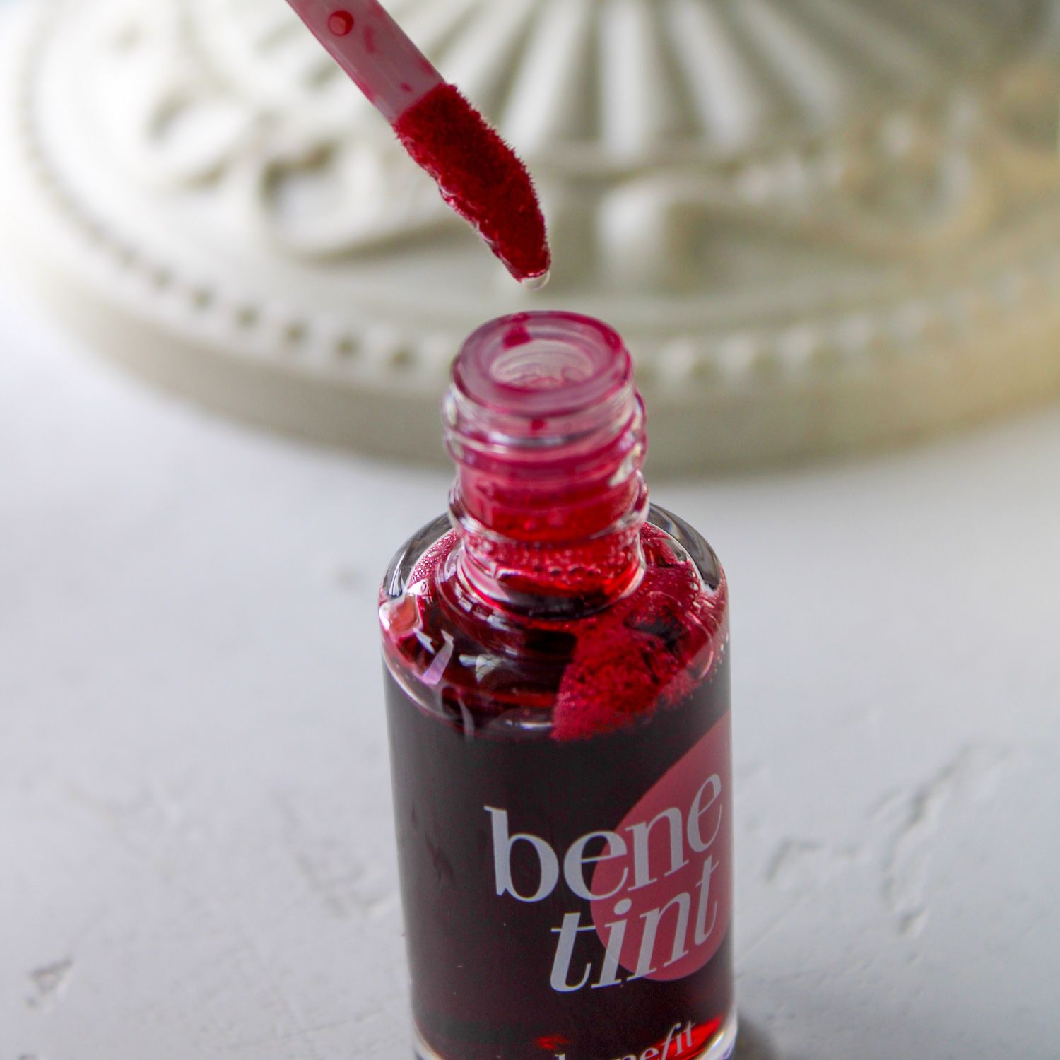 Close-up of Benefit Benetint lip and cheek tint bottle with applicator dipped in product