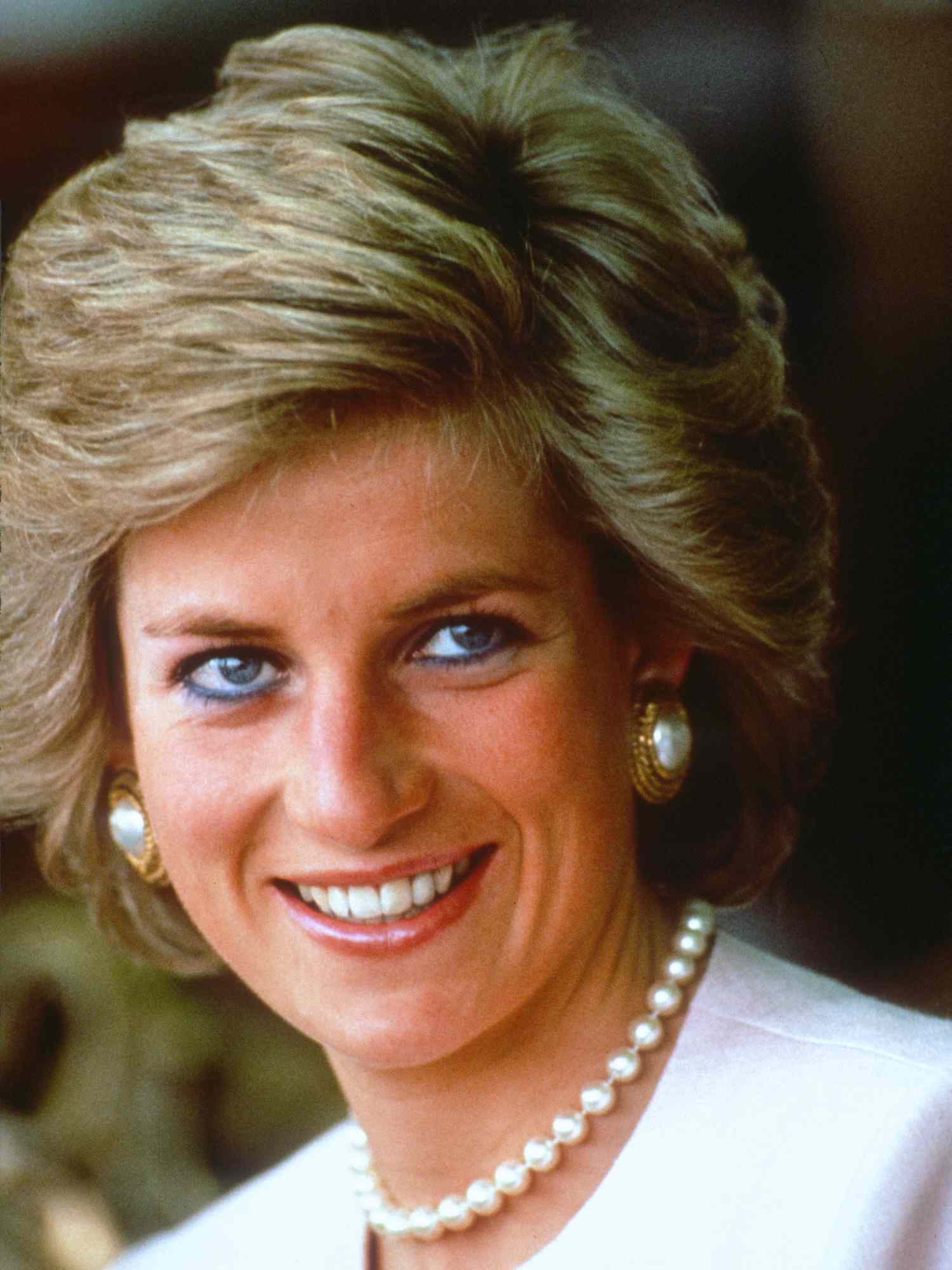 Princess Diana wearing a voluminous bouffant hairstyle, pearl jewelry, and a pale pink Catherine Walker suit