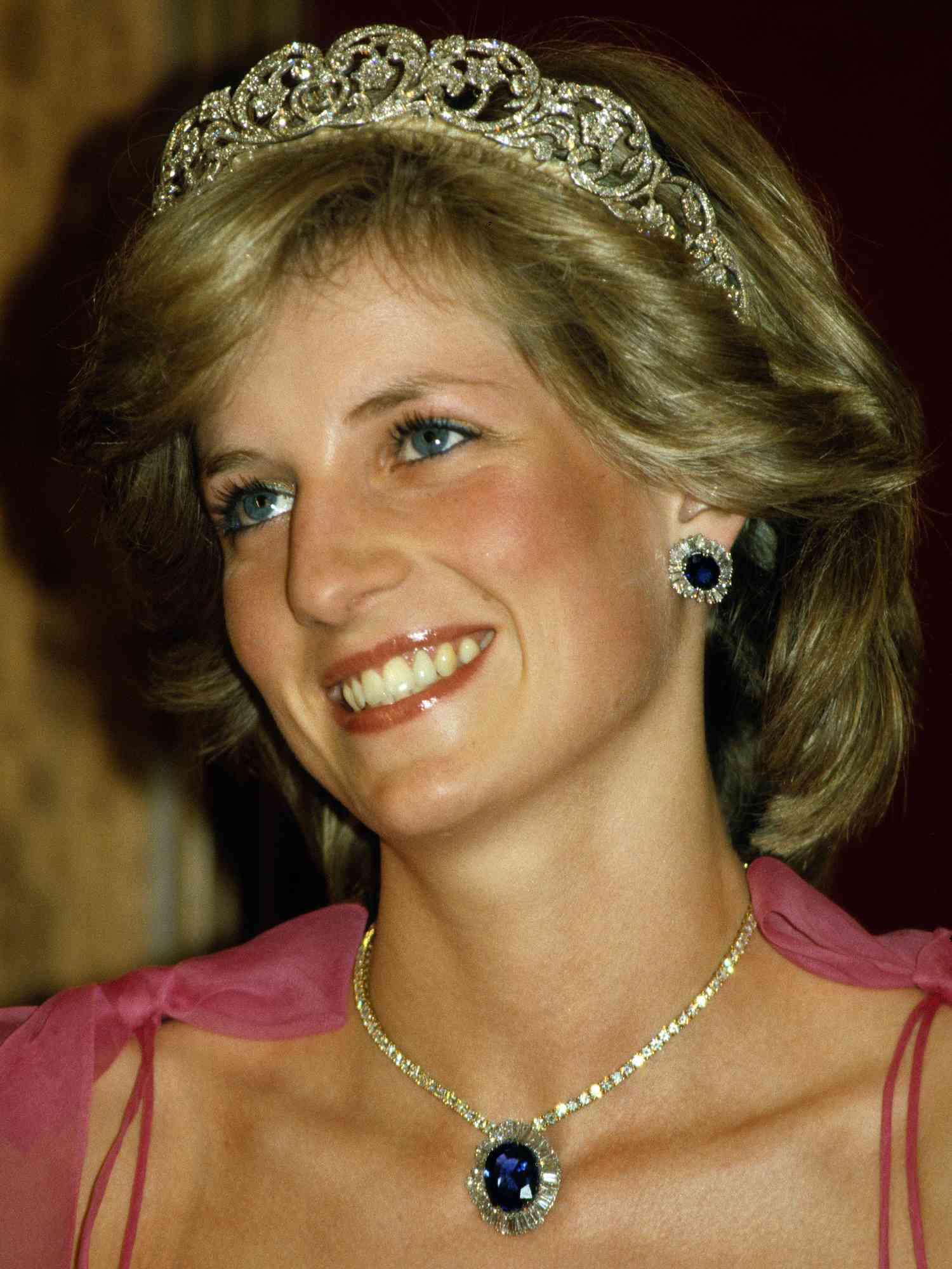 Princess Diana wears a voluminous short hairstyle, tiara, and pink dress