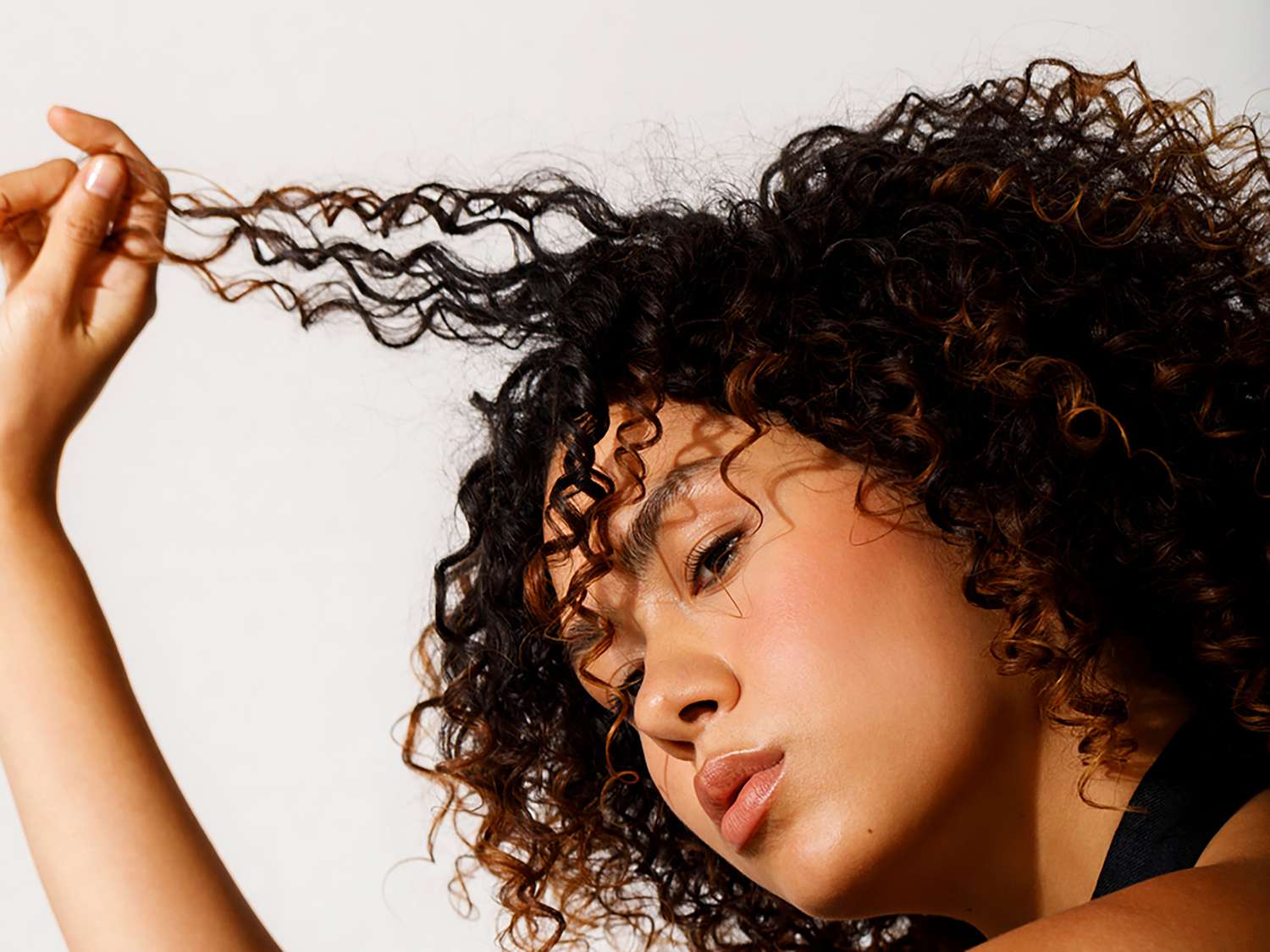 woman in profile, holding up a strand of her curly hair