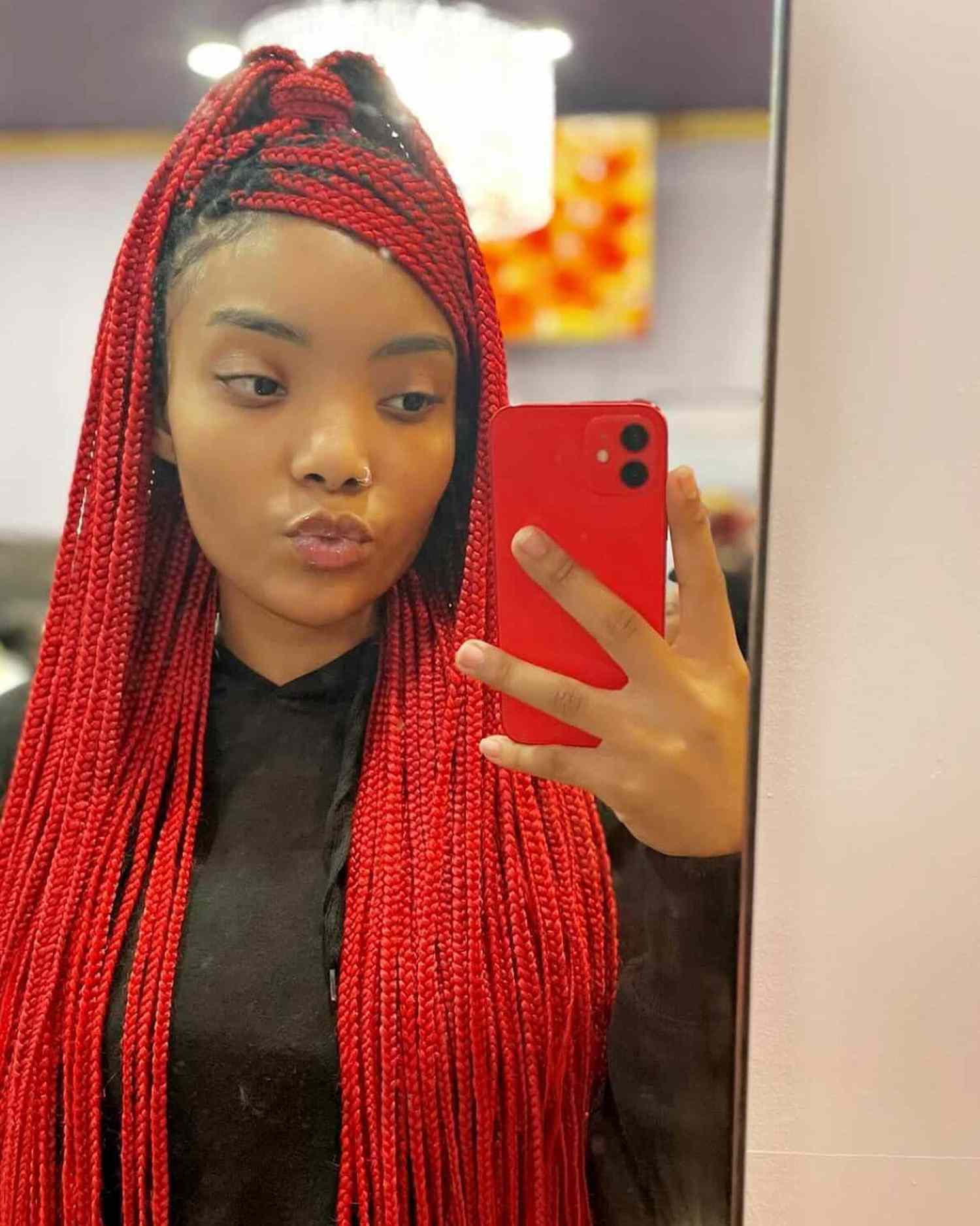 Red box braids in a half up ponytail, some braids pulled to the side to mimic bangs